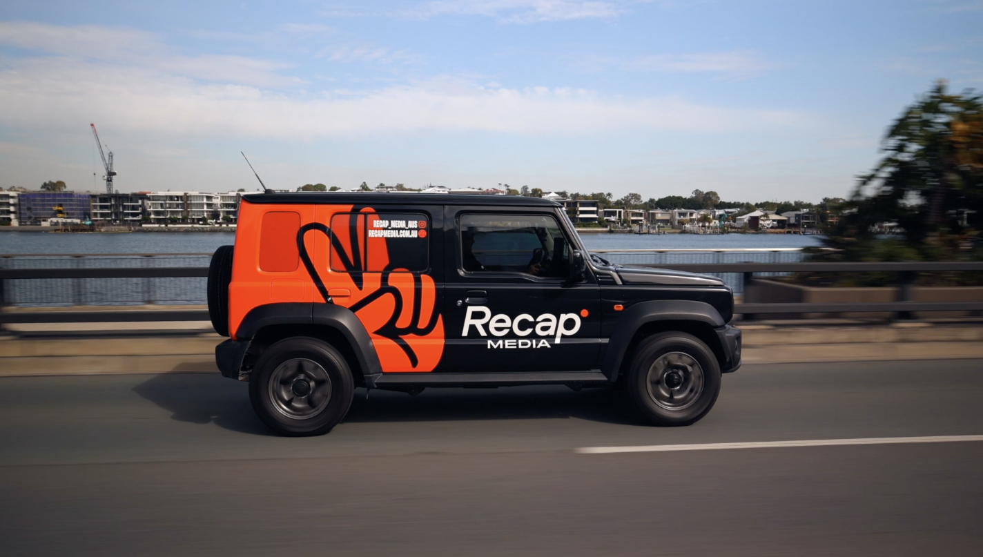 The Recap Media branded car with its orange hand wrap, driving across a Brisbane bridge
